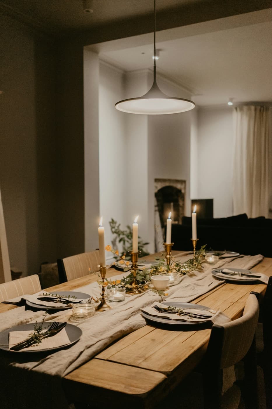 A candlelit dining table laid with linen, greenery and simple ceramics